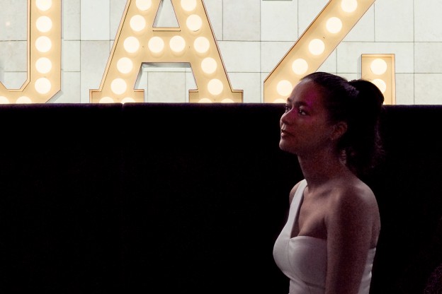 Close-up of a woman sitting in front of a huge, illuminated “Jaz” lettering.
