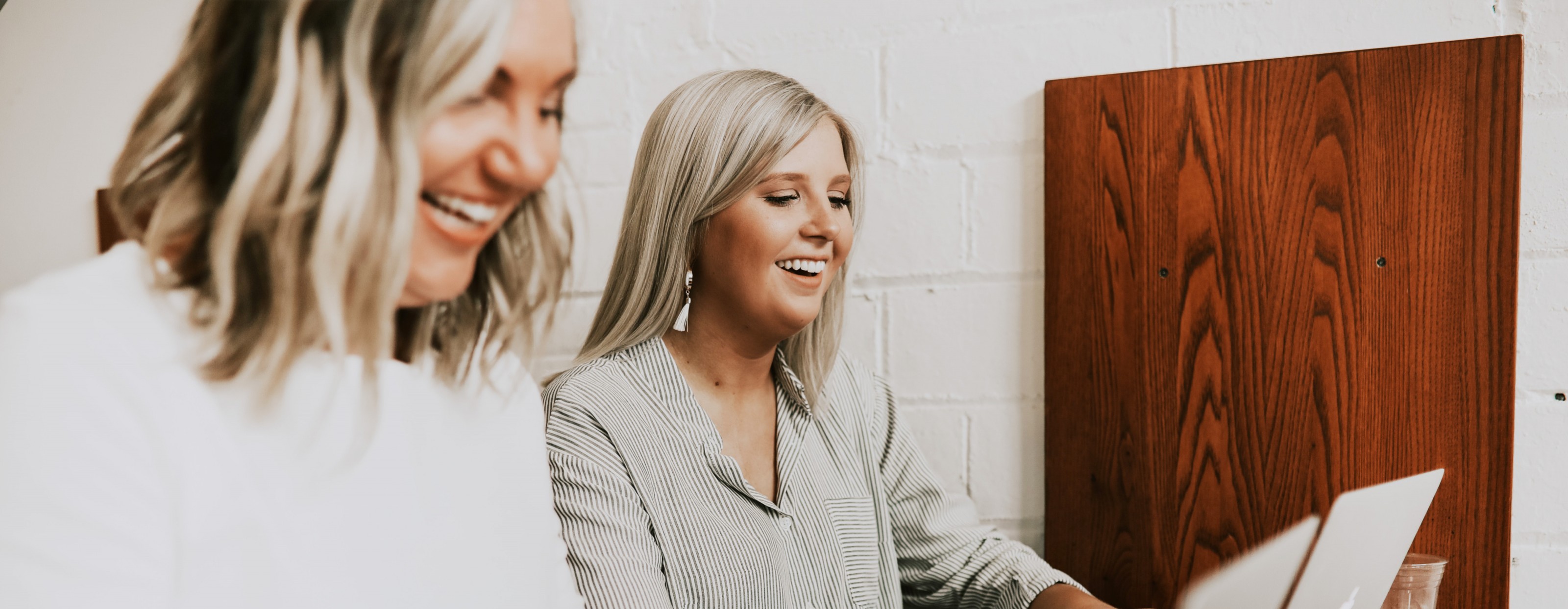 Two laughing employees are working side by side on their modern laptops.