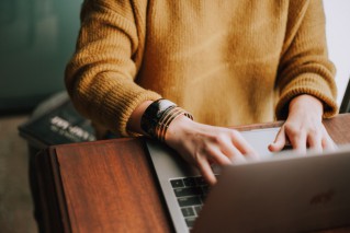 Close-up on the hands and arms of a young person, working on a laptop.