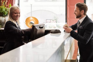 Eine junge Mitarbeitende begrüßt einen Geschäftsreisenden an einer modernen Hotelrezeption.