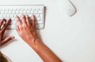 Nahaufnahme von zwei Händen, die auf einer kleinen, weißen Tastatur tippen.