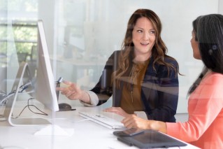 Two employees in a modern office space. They are looking at a computer screen, discussing their work.