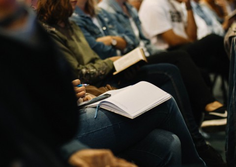 Detail shot of a conference situation. Mpeople are seated next to each other, taking notes.